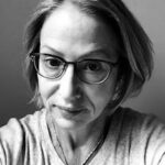 Black and white headshot of Kim Eggers, who is smiling and wearing glasses.