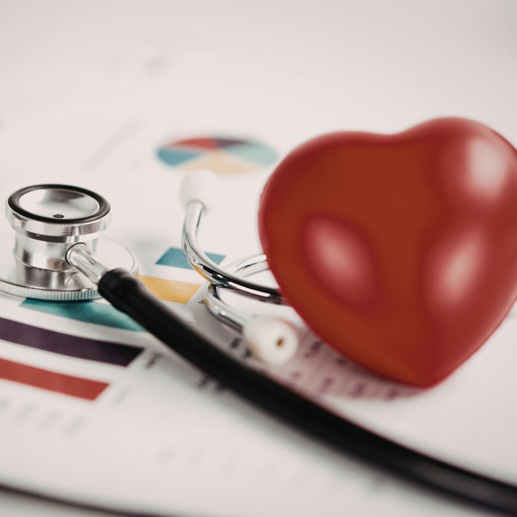 Close-up of a stethoscope beside a red heart-shaped model on top of a medical chart.